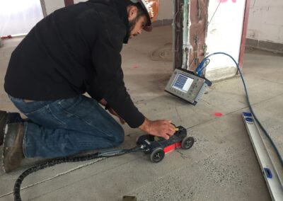 A worker wearing hard hat and black long sleeves pushes a device with four small wheels while watching the monitor attached to the device,