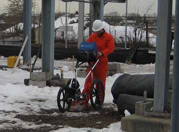 A worker wearing safety gear scanning the ground amid the snow.