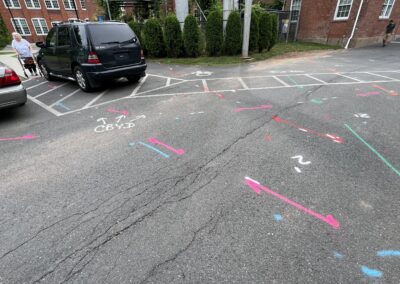 A driveway with blue and orange markings on the ground with parked black and gray cars in the corner.