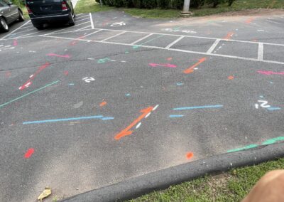 A driveway with blue and orange markings on the ground with two parked gray and black cars on the left side of the driveway.