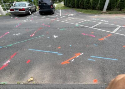 A driveway with blue and orange markings on the ground with two parked gray and black cars on the left side of the driveway.